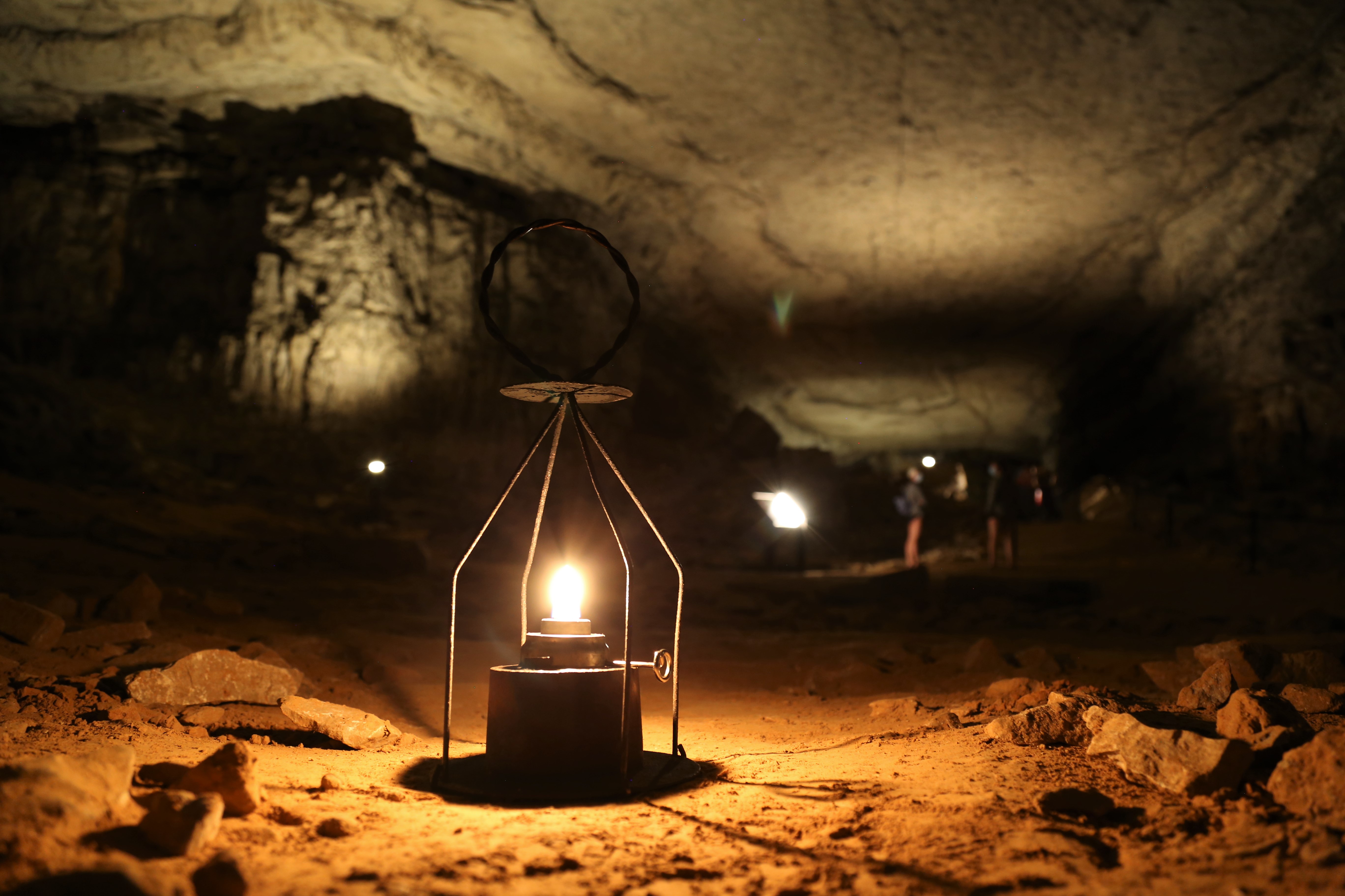 An open flame wire lantern glows in a large dark and rocky cave room