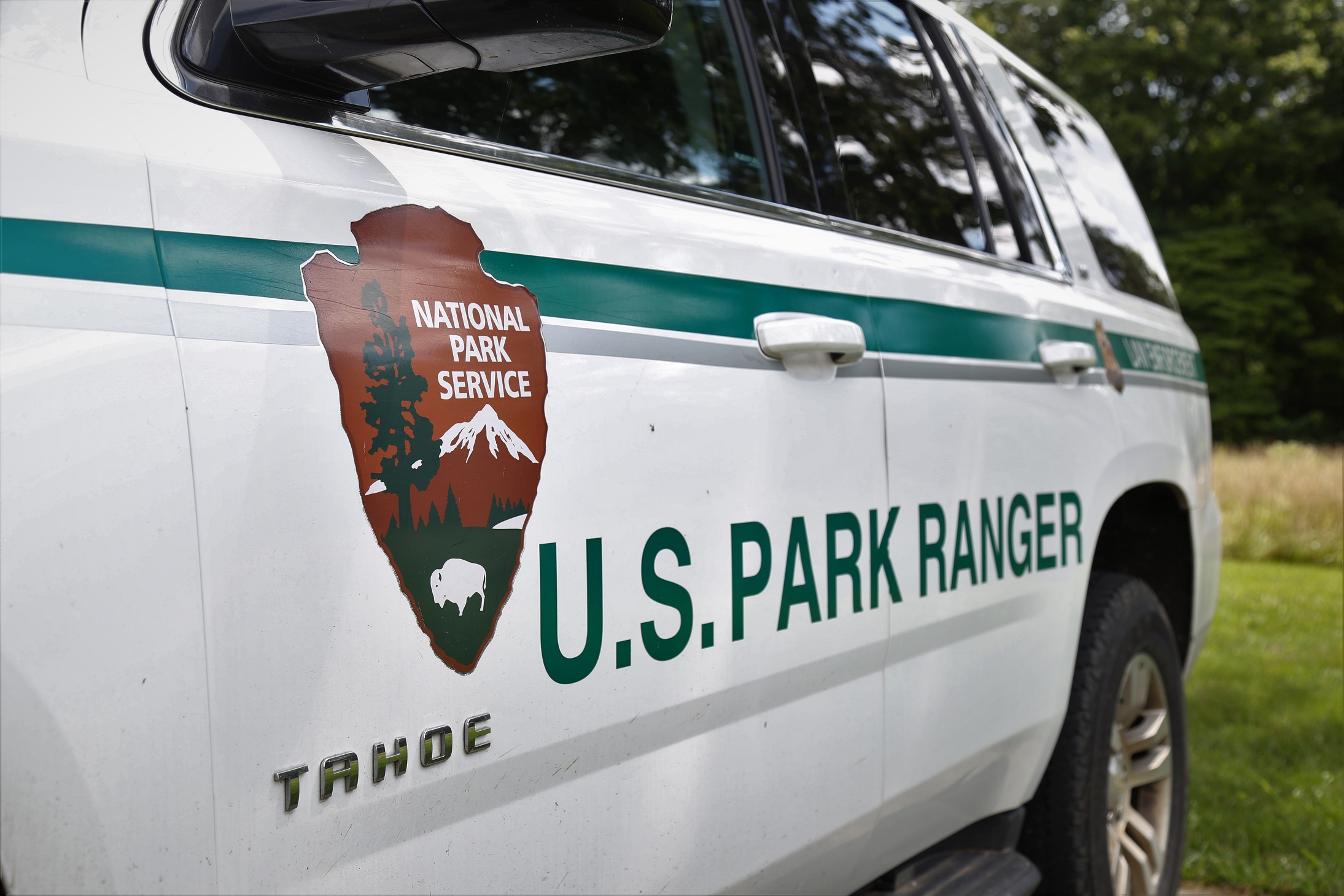 National Park Service Arrowhead Logo and U.S. Park Ranger written on the side of a white SUV.