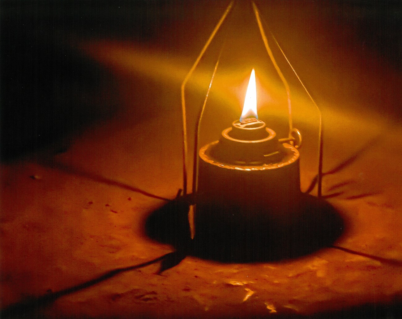 Close-up photo of a simple candle style lantern, the orange flame casts shadows and creates a halo.