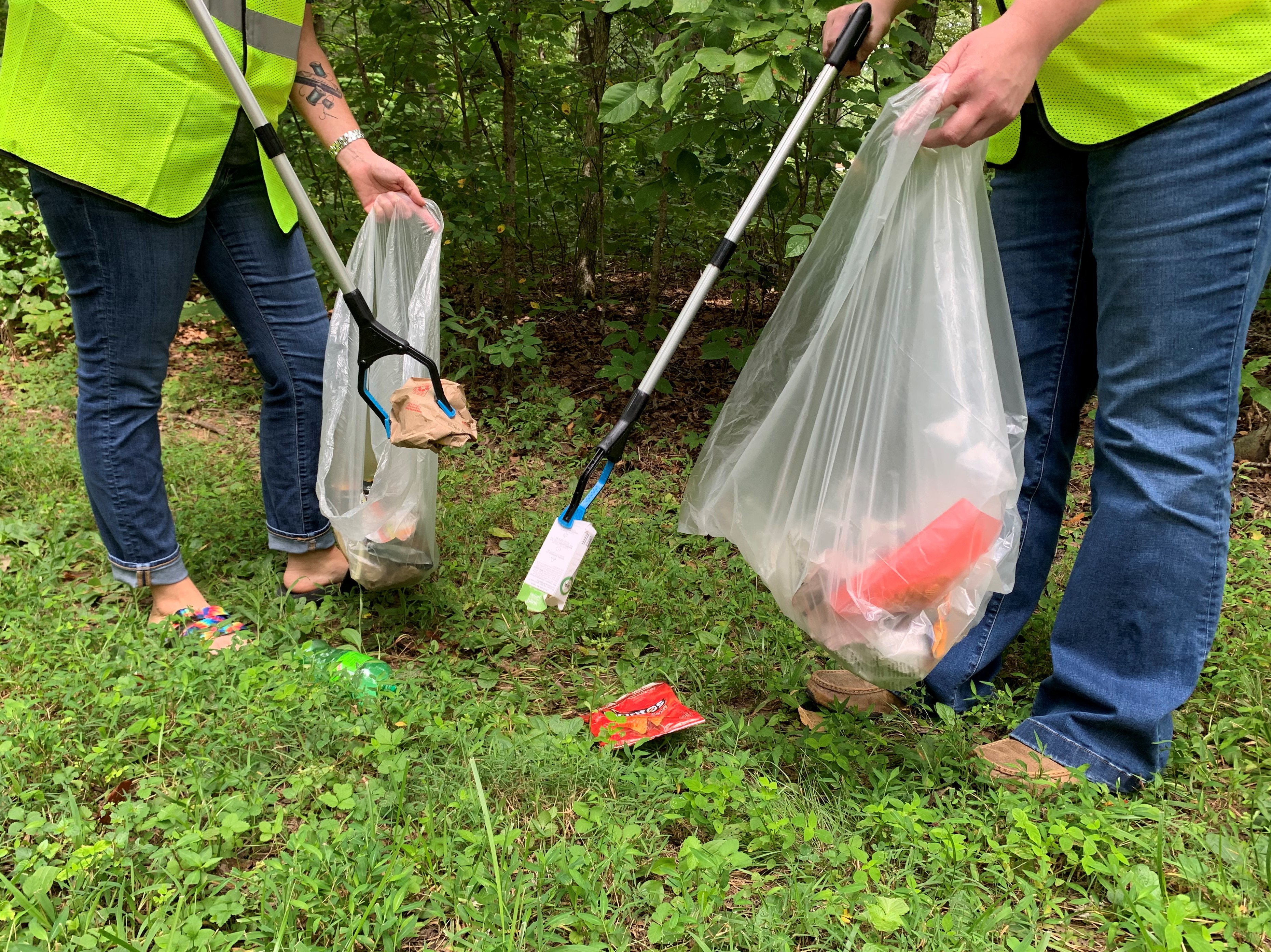 Mammoth Cave National Park will host a volunteer litter clean-up event on April 22, 2025. Two people wearing high visibility vests are shown from the waist down as they use tools to pick up litter from the ground.