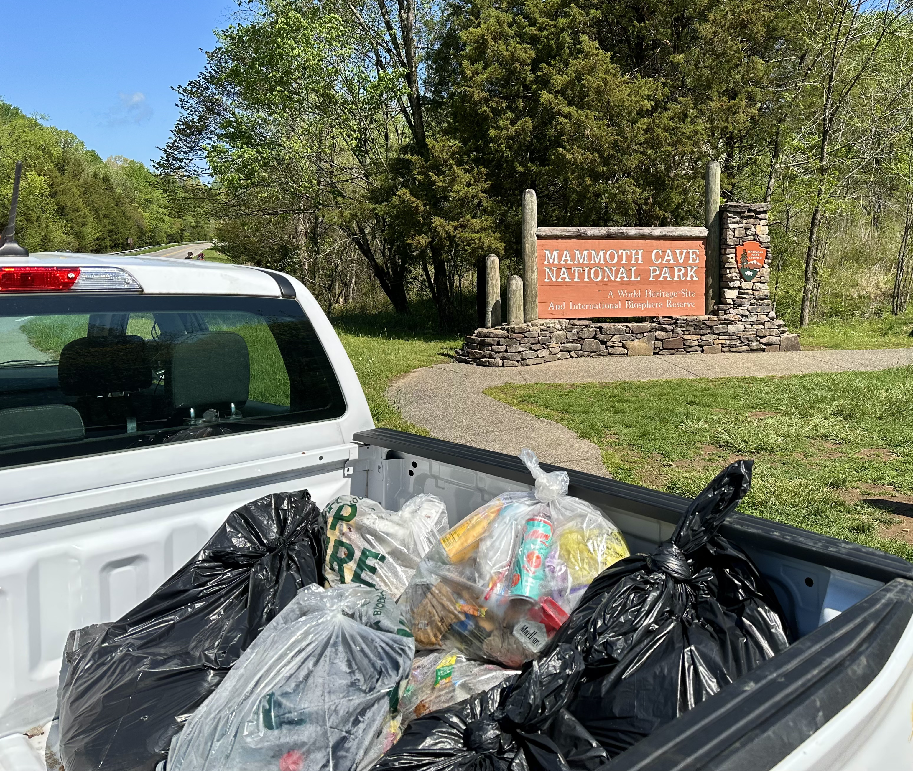 Mammoth Cave National Park Earth Day Volunteer Event Trash Pick Up The back of a pickup truck filled with trash is visible in front of a large wood and stone sign that says, “Mammoth Cave National Park.”