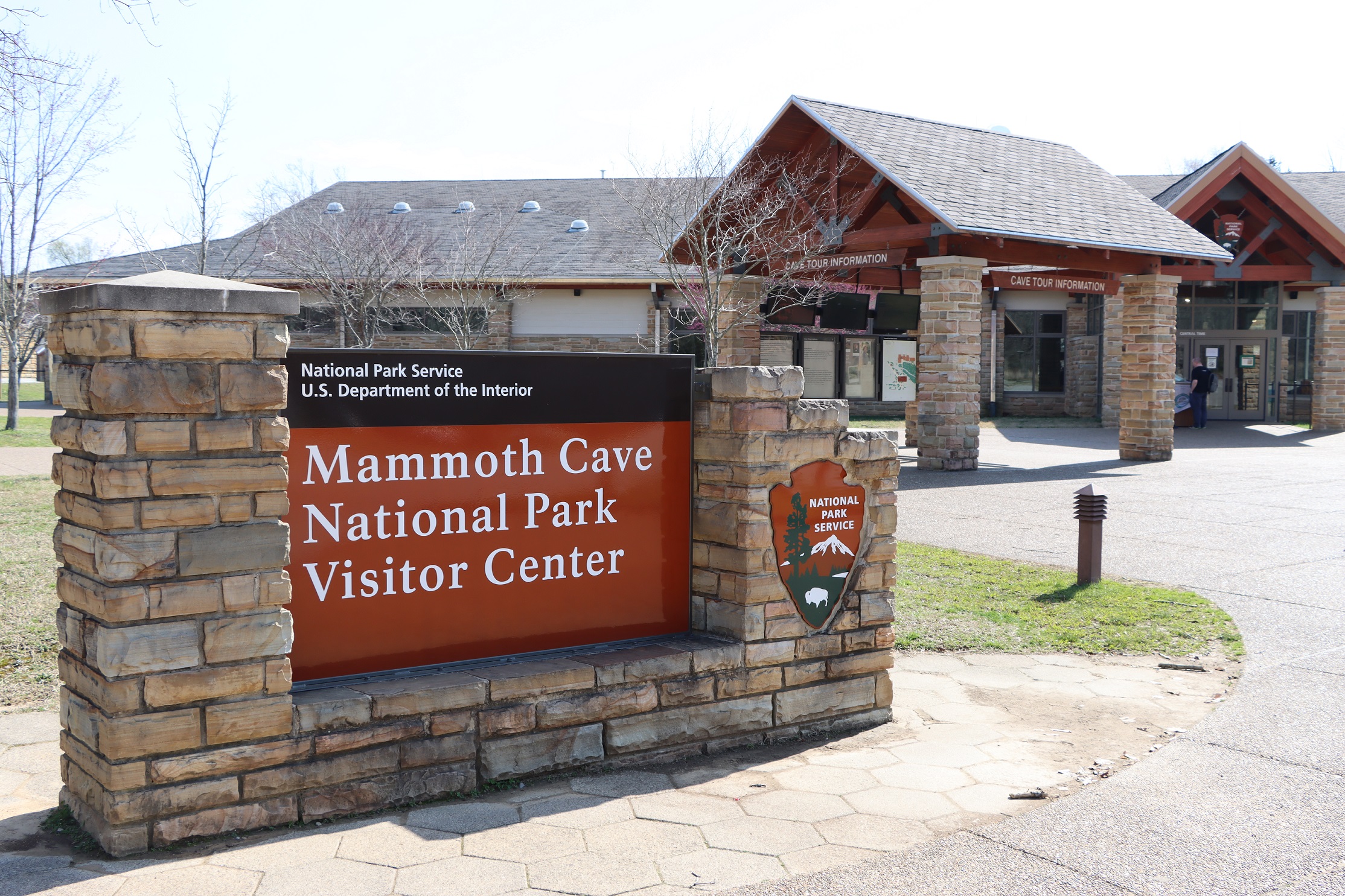 A sign says "Mammoth Cave Natioal Park Visitor Center" stands in front of a large stone building.