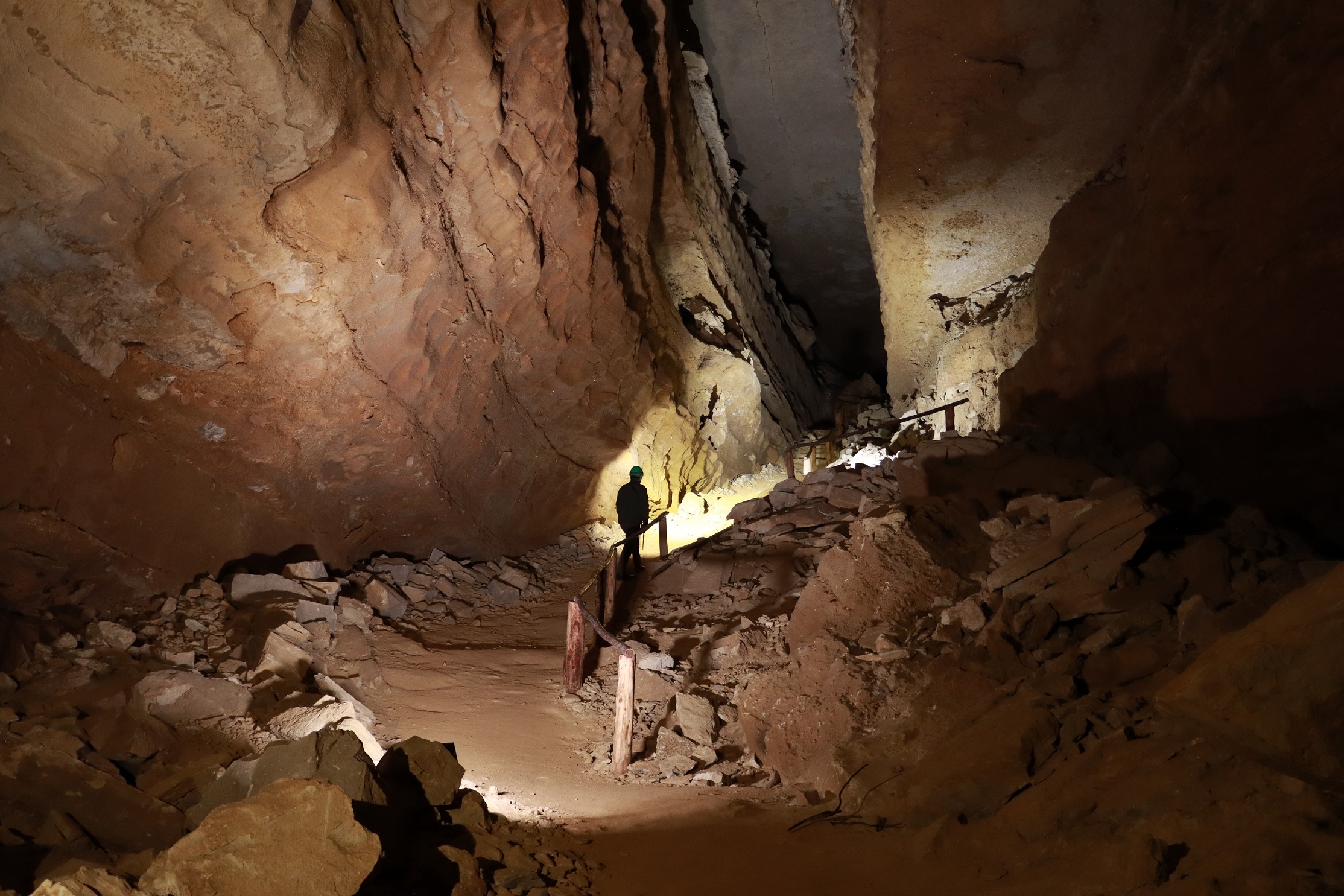 Crystal Cave was first discovered by famous cave explorer Floyd Collins in 1917. It was connected to the Mammoth Cave system by members of the Cave Research Foundation in 1972. A person climbs a steep hillside in a dimly lit cave passage.