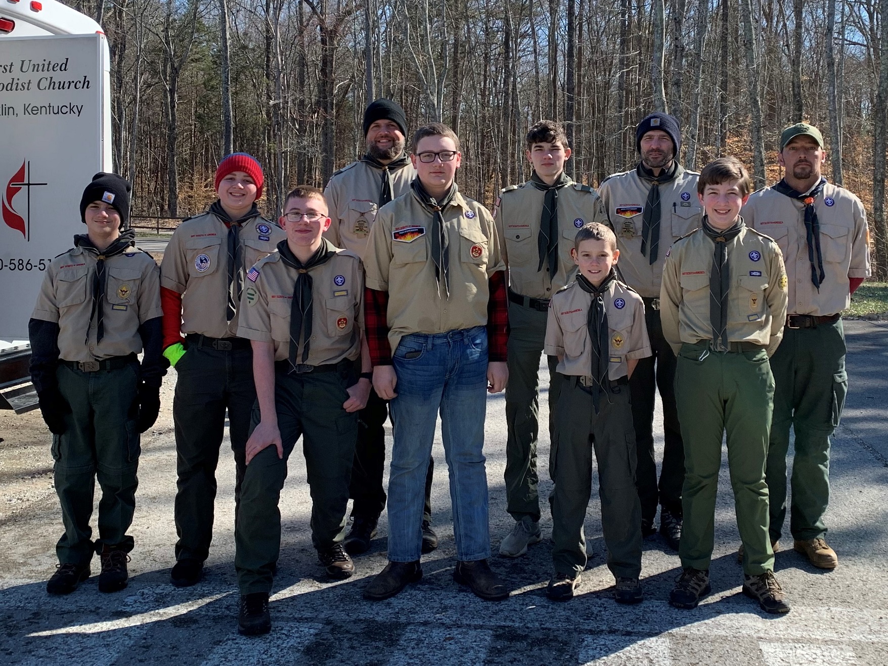 Several Boy Scouts and their Troop leaders stand side by side for a group photo.