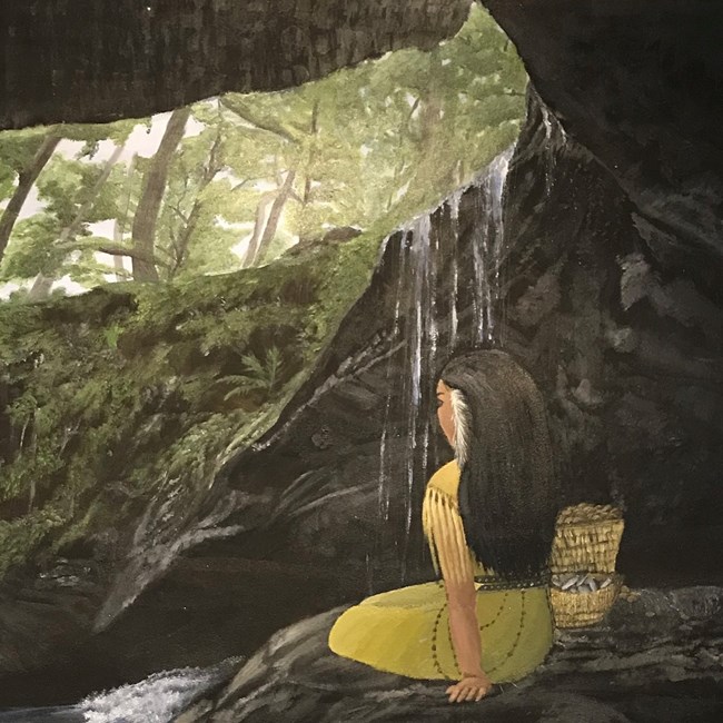 A woman sits in a dark cave with water flowing over the mouth of the cave while a green forest is visible in the cave opening above.