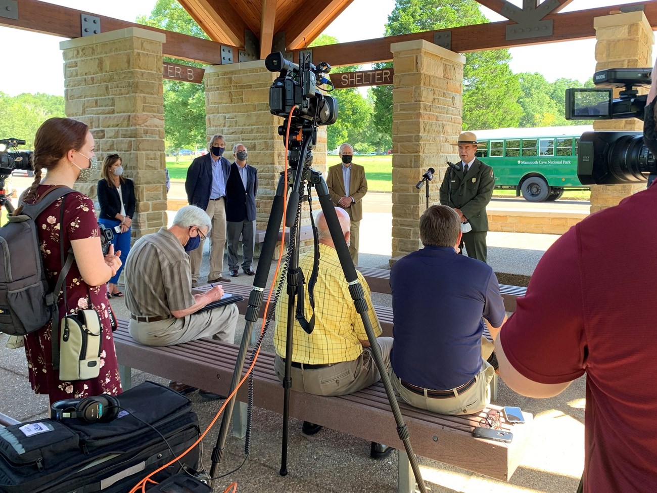 Several reporters with video cameras film a ranger wearing the NPS uniform and flat hat as he speaks into a microphone at an outdoor news event.