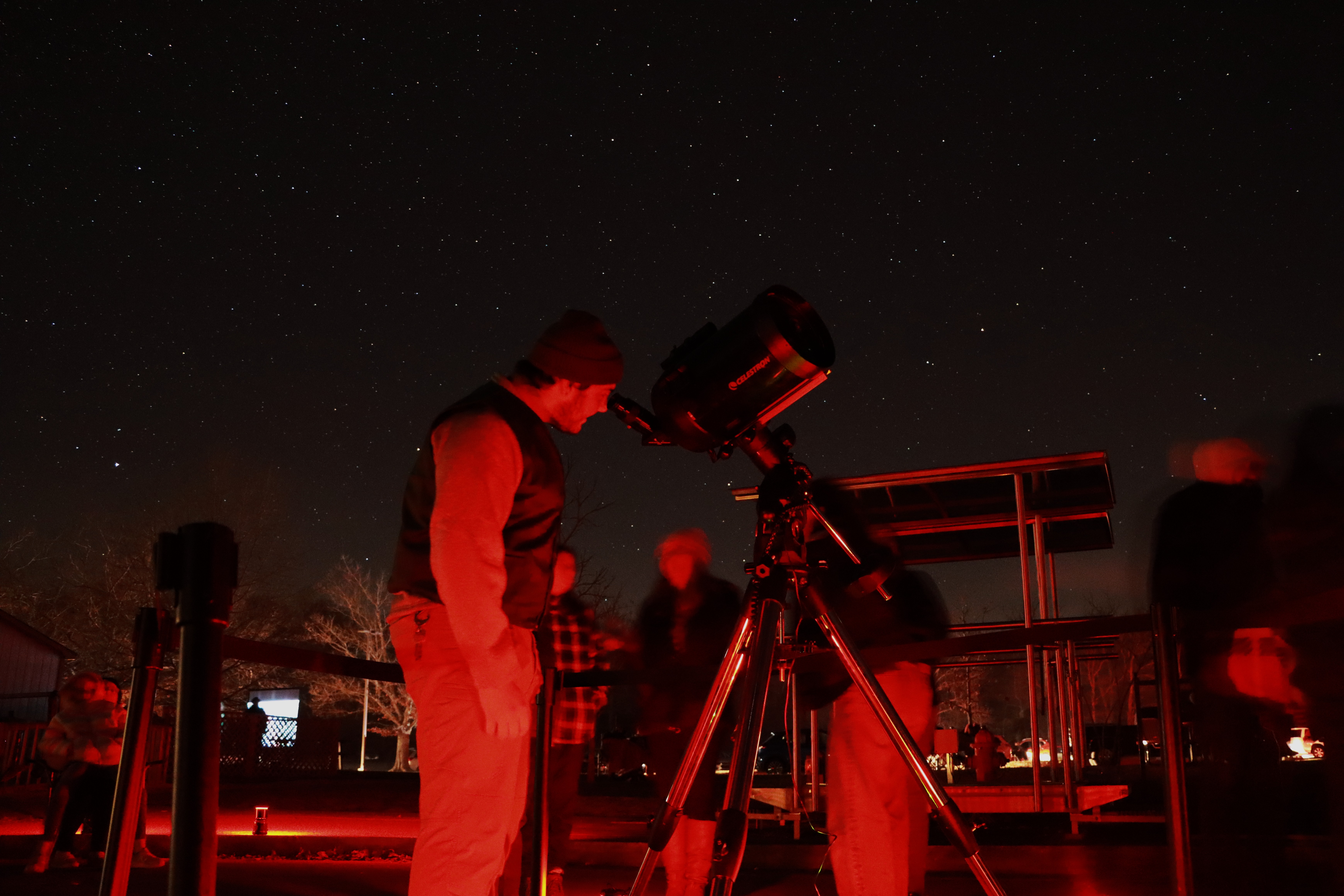 A person is illuminated by red lighting as they look at the night sky through a large telescope.
