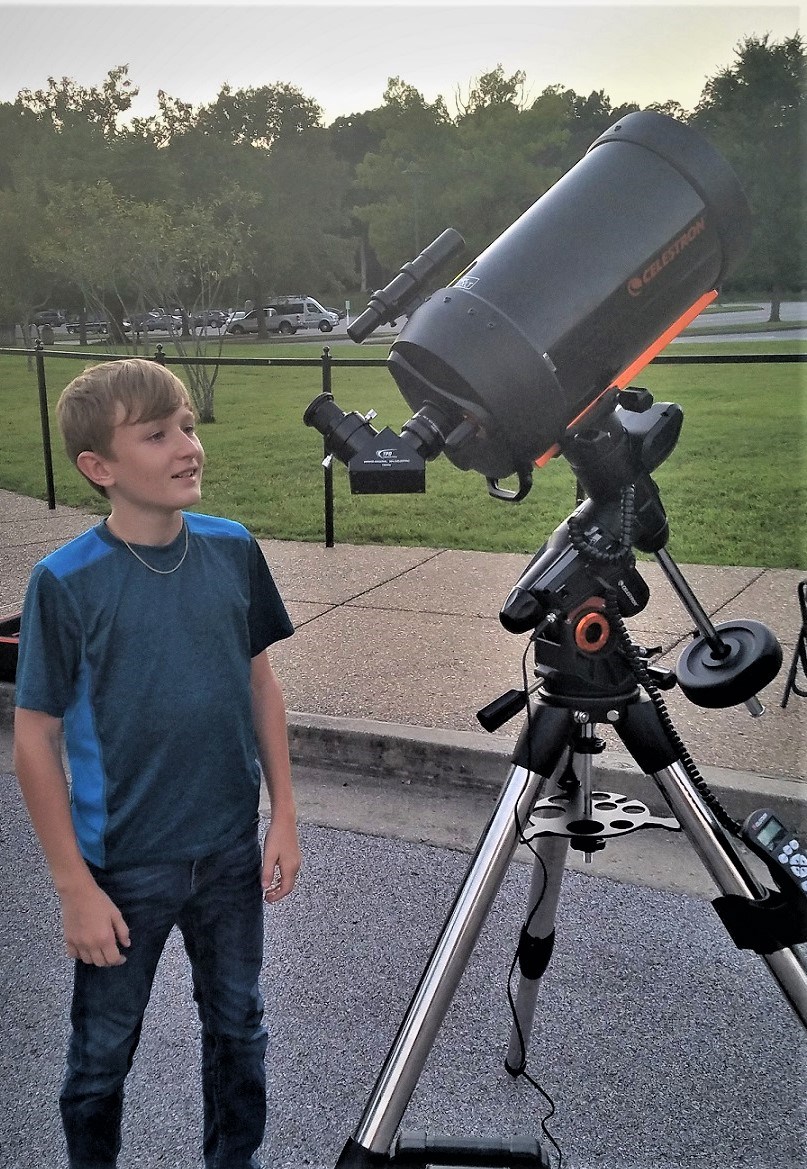 A child stands next to a very large telescope.