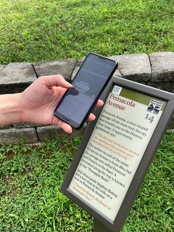 Someone uses their cell phone to scan the QR Code on a Beneath Your Feet sign