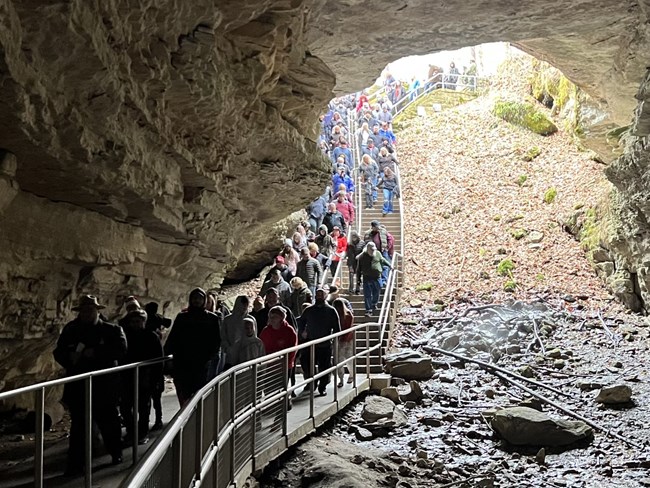 A croud of people walk down a long staircase into a cave.