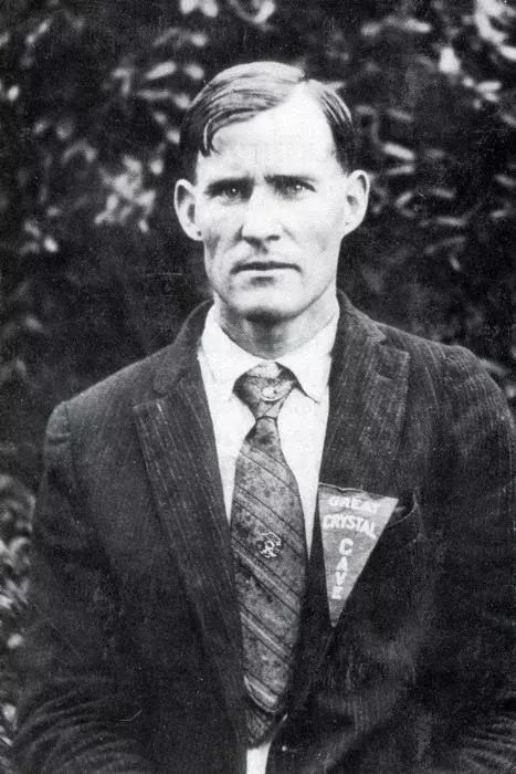 A historic photo of a man wearing a suit jacket and tie wears a pennant on his lapel with text “Great Crystal Cave”.