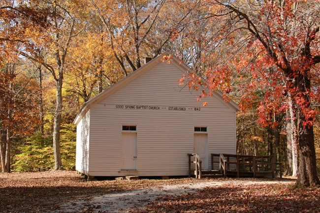 A simple white church building with red and orange leaves all around.