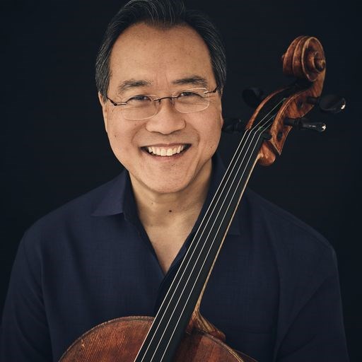 A man smiles as the neck of a cello is visible across his chest.