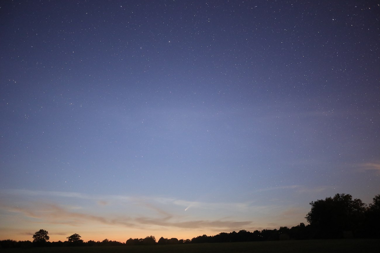 A small streak of a comet along the bottom of the sky with stars above.