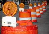 Line of orange traffic barrels with warning flashers on the top.