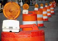 Line of orange traffic barrels with warning flashers on the top.