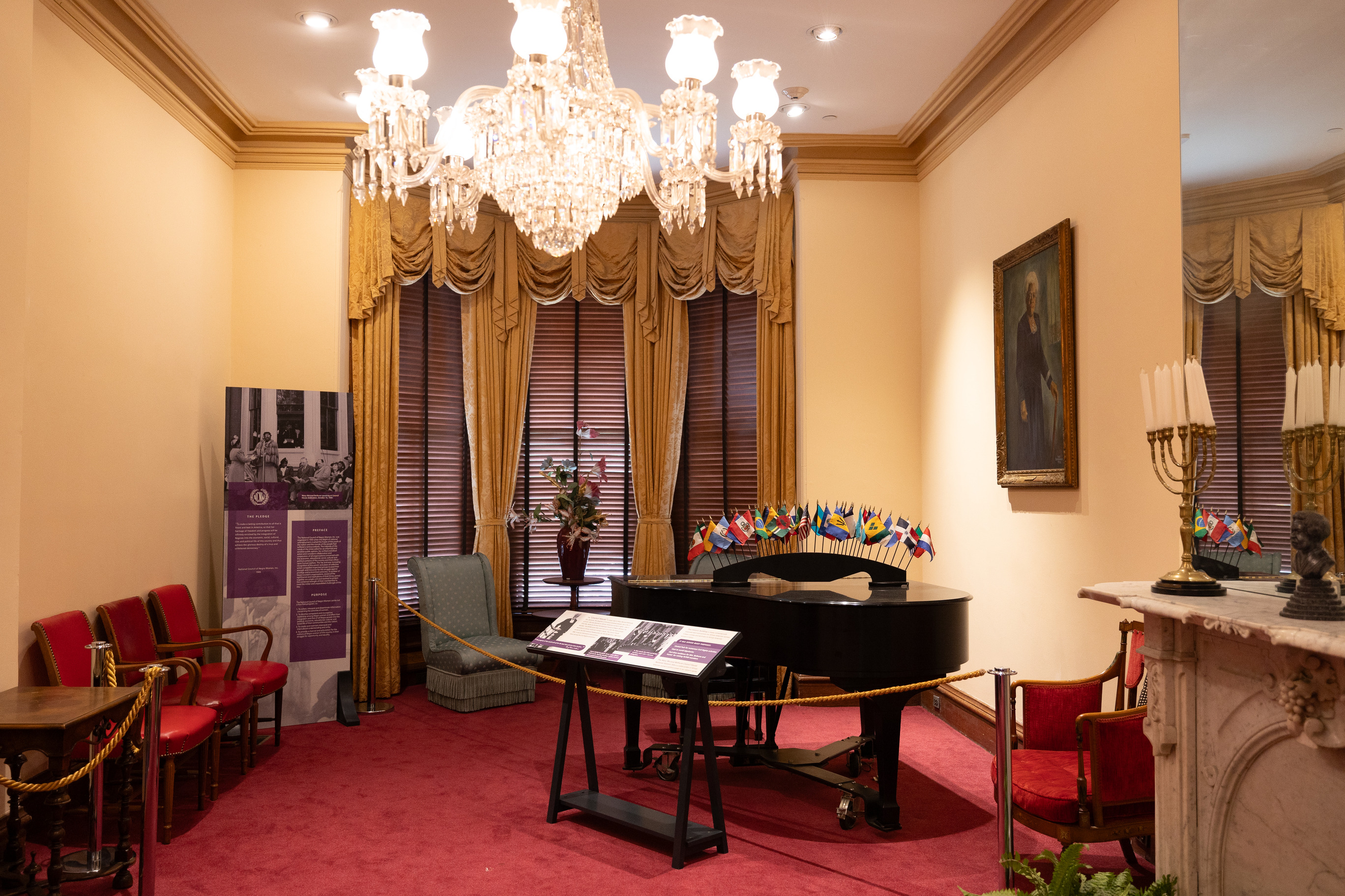 A view of the parlor at Mary McLeod Bethune Council House National Historic Site, featuring a glowing chandelier and piano on red carpet.