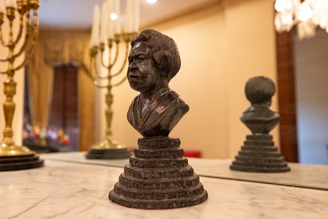 A miniature statue of Mary McLeod Bethune sits on a ledge in front of a mirror. A menorah stands in the background.