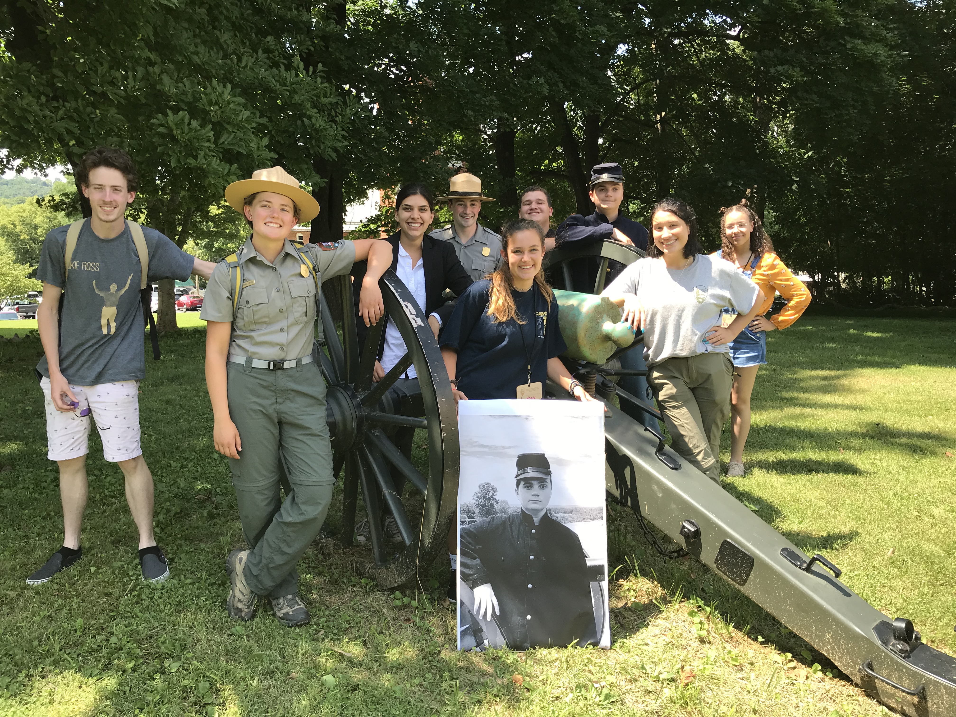 Various youth staff pose for a photo next to an artillery piece in costume after performing a skit.