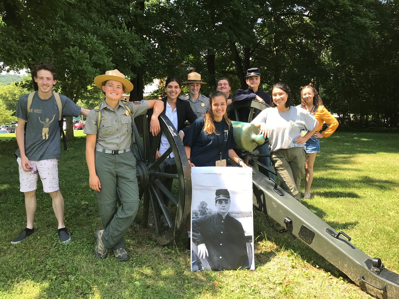Various youth staff pose for a photo next to an artillery piece in costume after performing a skit.