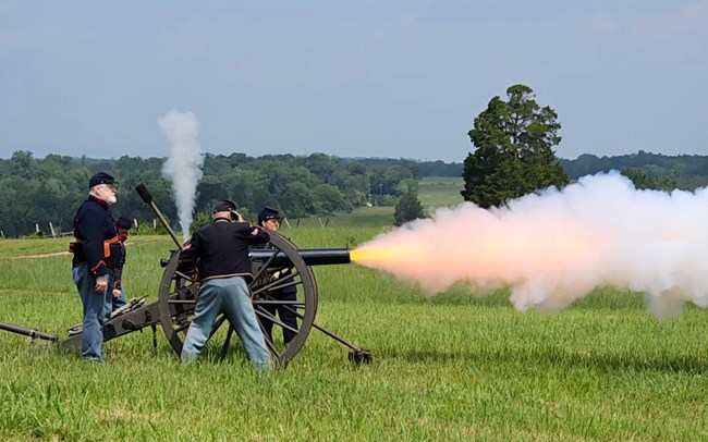 Living Historians fire a cannon in Civil War Uniform on Henry Hill. Fire and smoke stream out from the barrel and vent.