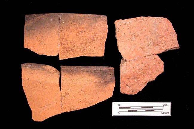 Color image of three broken pieces of terracotta-color pottery on a black background.