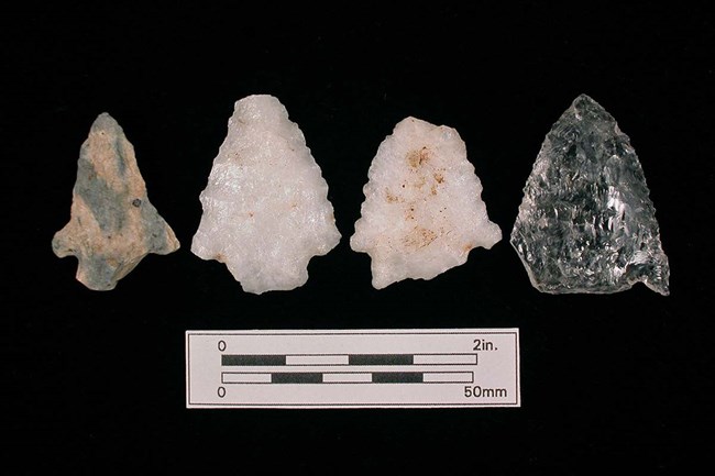Color photo of four different arrowheads on a black background. The first is a dark gray color. second and third are white, and fourth is dark gray.