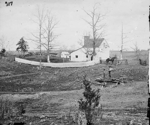 Black and White photo of the Thornberry House in 1862. The white wooden house stands in the middle of the image, with a white fence and a few outbuildings. The landscape is faitly bare, with no grass and few trees. Two individuals stand with a horse behin