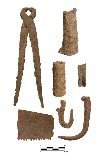 Color image of rusted tools on a white background. Some tools are complete while others are just pieces. The tools include a pair of pincers, a saw blade, and a knife blade.