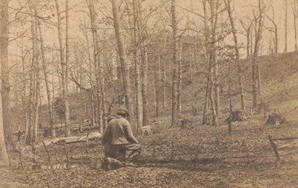Two boys kneeling at the grave of a soldier, surrounded by trees with leaves littering the ground.