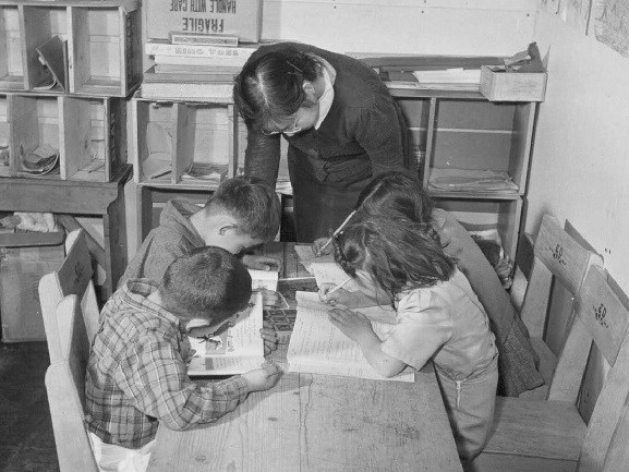 Teacher leans over two children writing at a table
