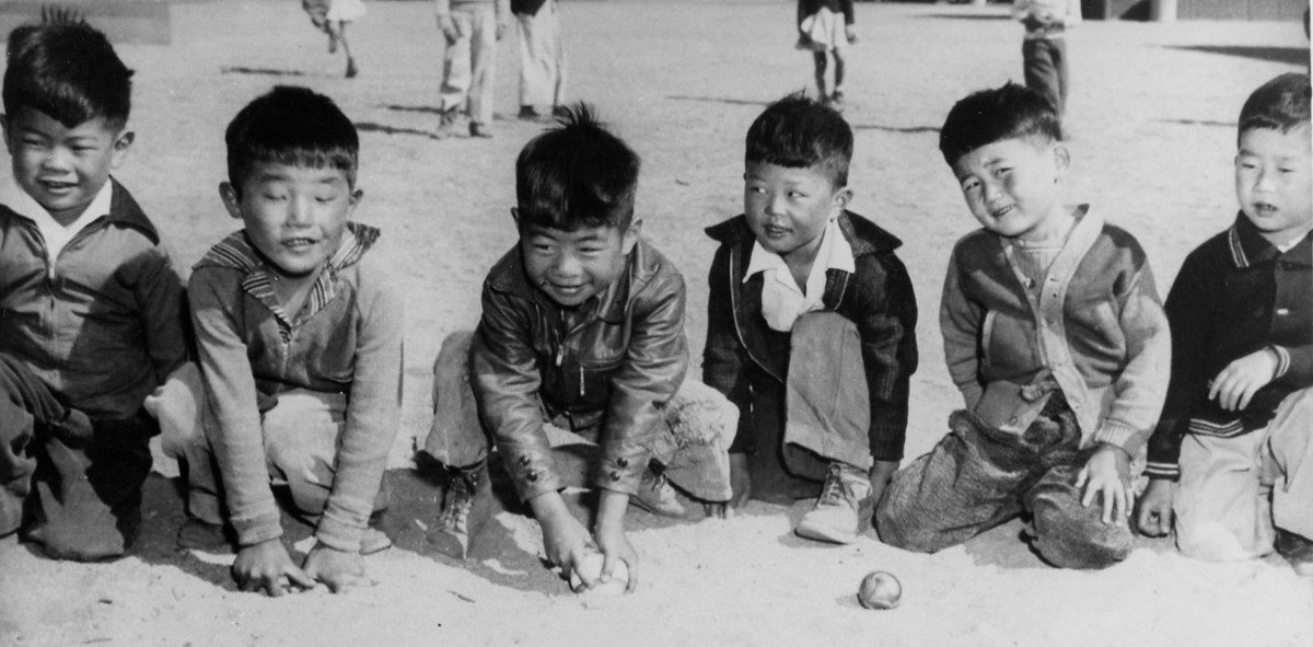 Six little boys play in dirt with marbles
