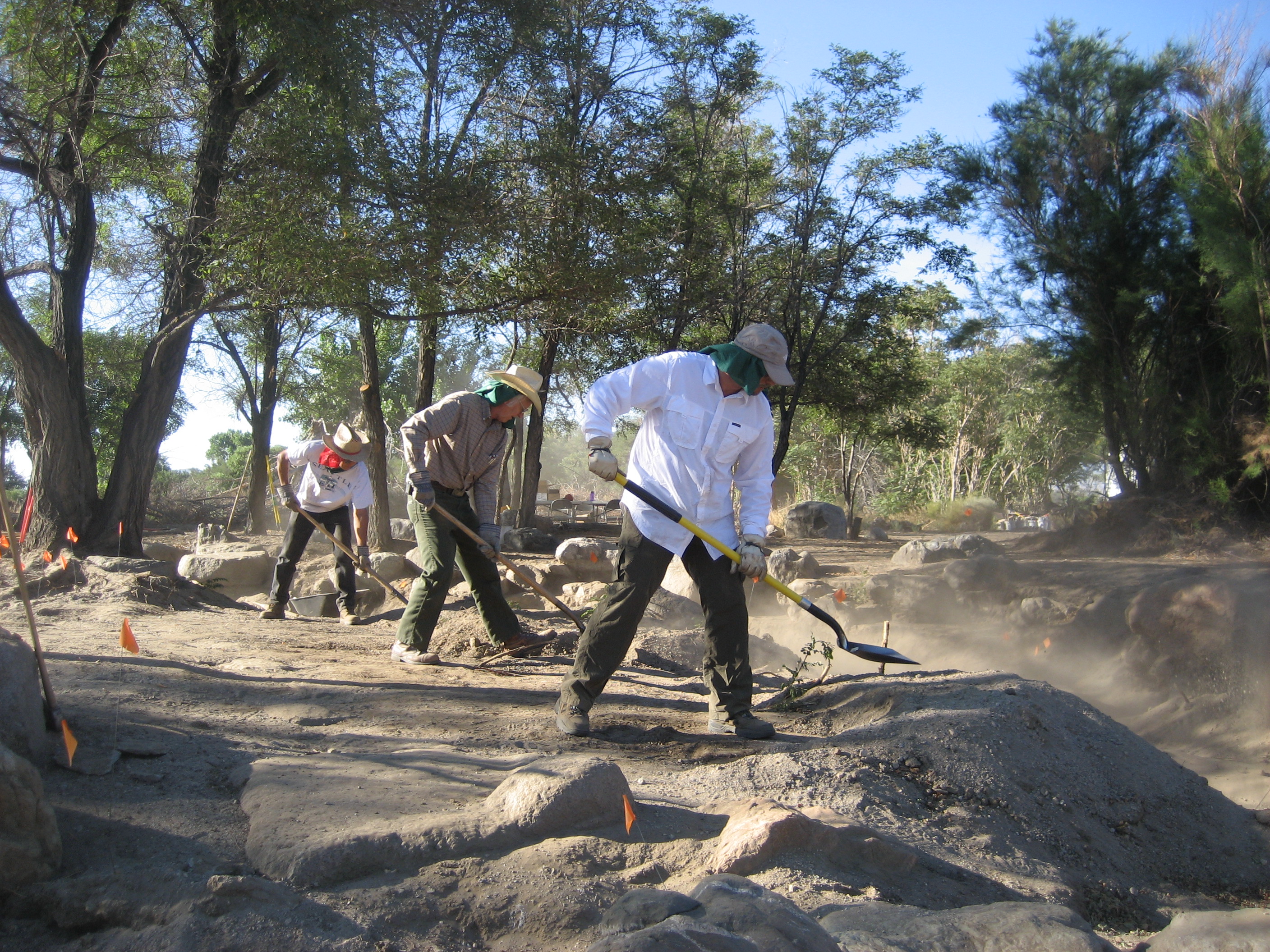 Dust flies as three volunteers with shovels dig out the upper pond at Merritt Park