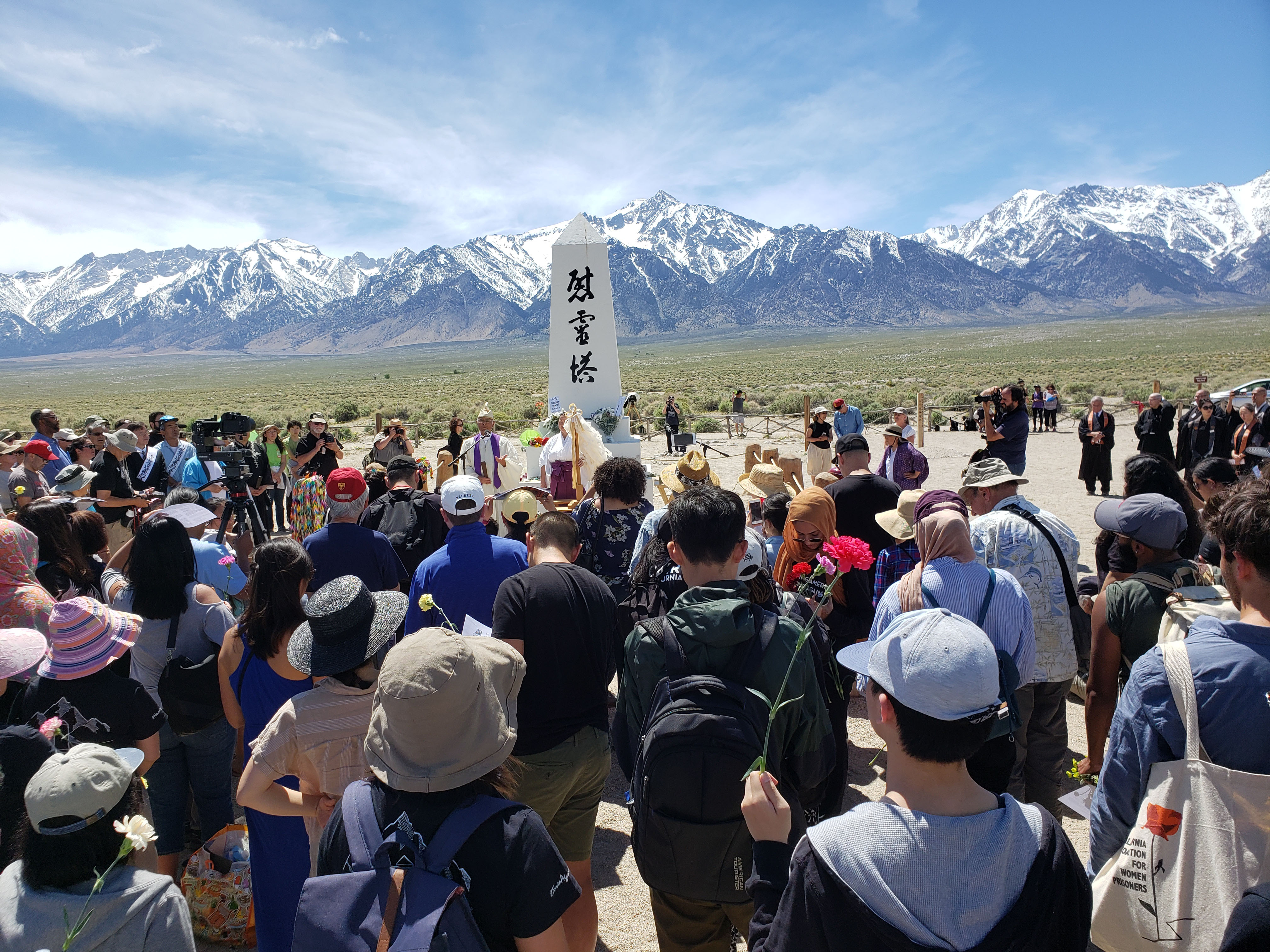 2019 Manzanar Pilgrimage crowd of people surrounding white obelisk with mountains in background
