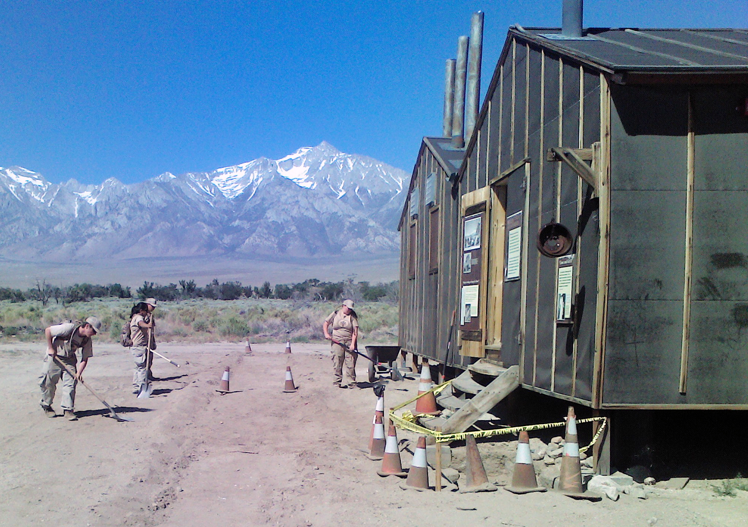 Manzanar YCC 2019 Mess Hall sidewalk crew works on tarpaper building with mountains behind