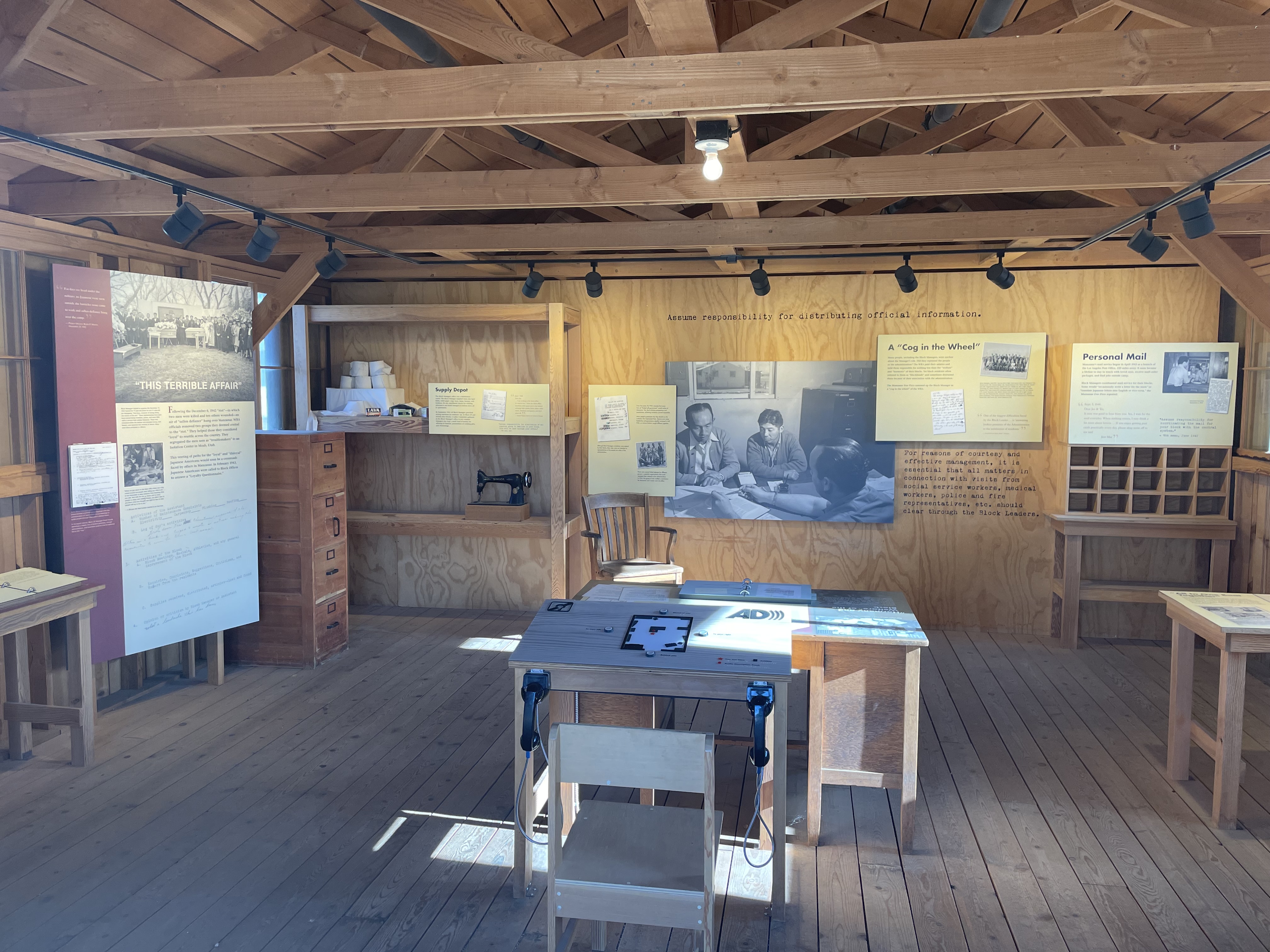 unfinished interior of wooden building with desk in the center and exhibits on walls