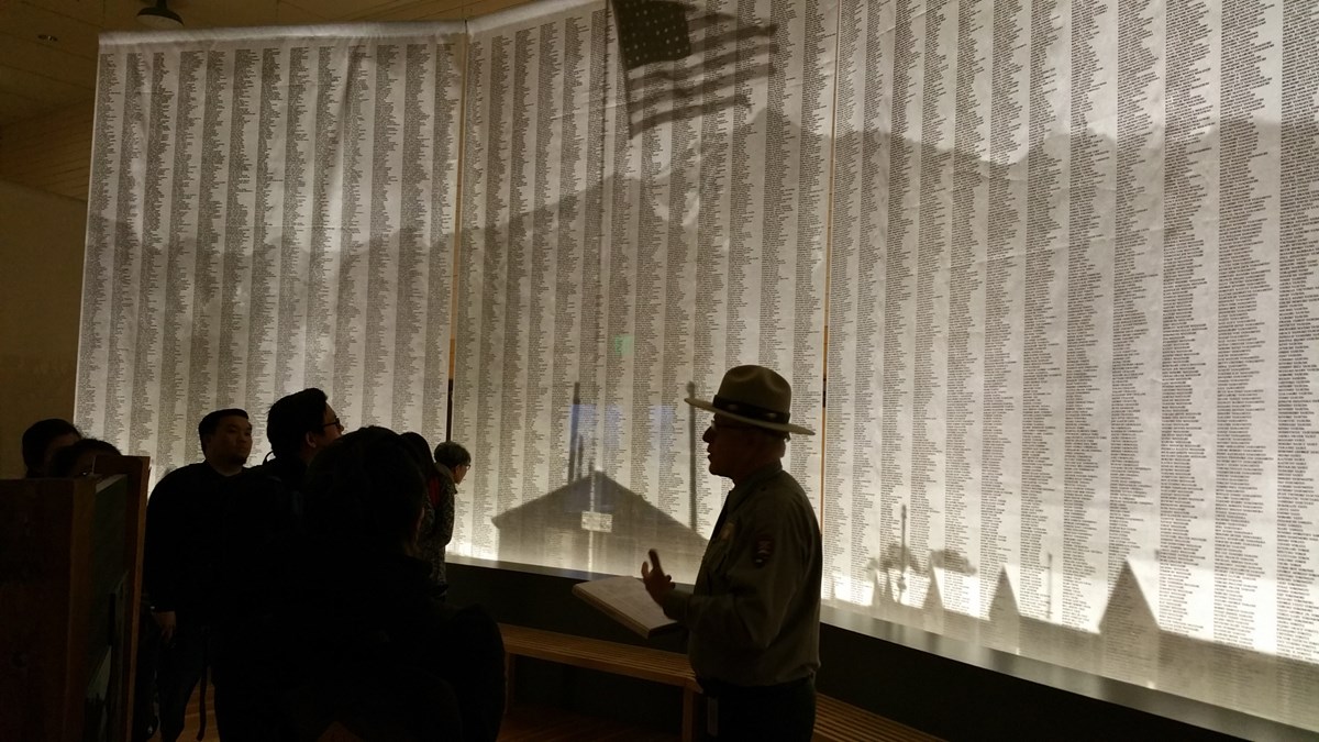 Shadow of Ranger talking to visitors in front of wall of  names