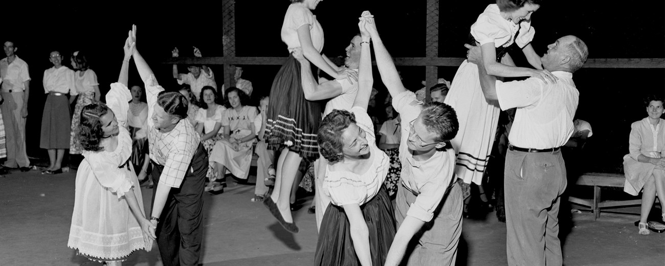 Black and white photo of several people dancing, hands clasped.