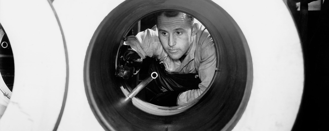 Black and white photo of man peering through equipment that are large circles.