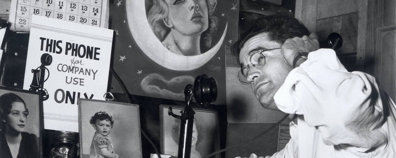 Using the phone in Oak Ridge, 1944 A man speaks on the telephone in an office with photos and a calendar on the wall.