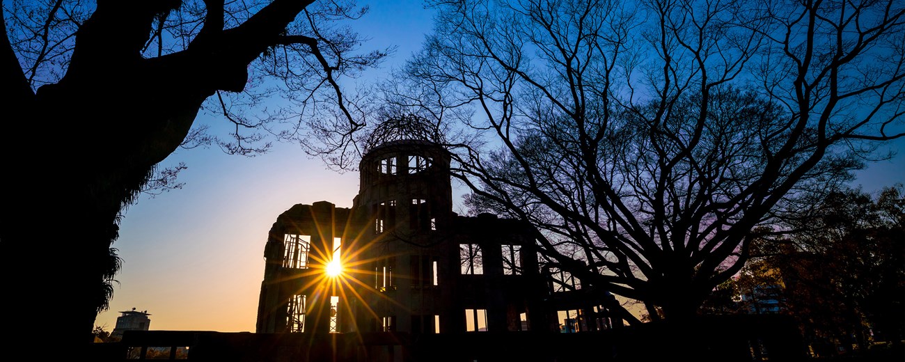 A color photo of a building in ruins that is silhouetted against the sun. The sun is shining through the building where a window used to be.