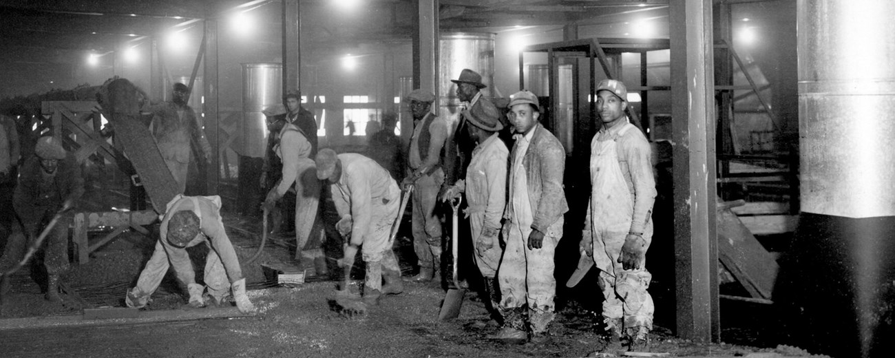 Several African American men with shovels in a long hallway.