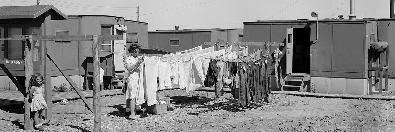 Black and white photo of a woman tending to laundry on a clothesline.