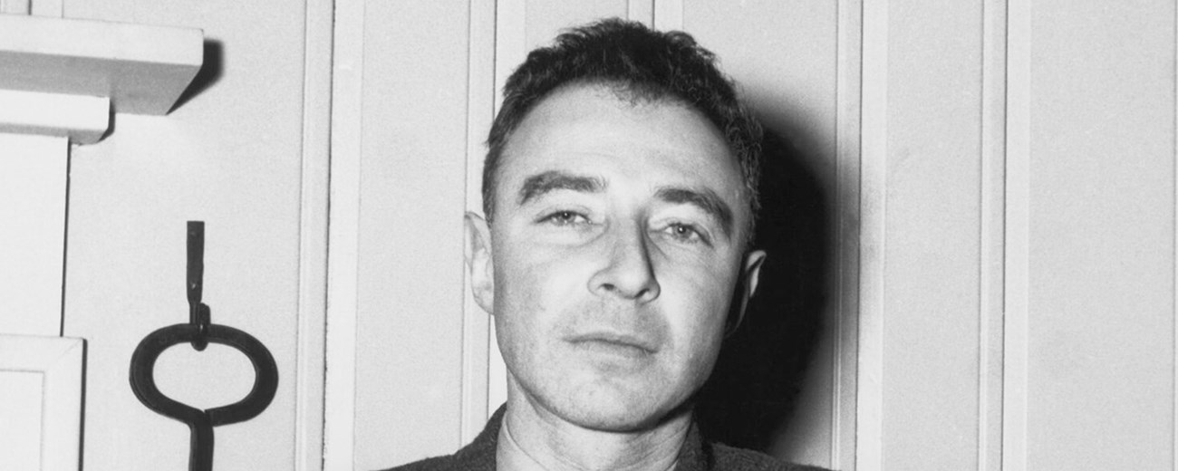 Black and white photo of Oppenheimer seated, staring at the camera.