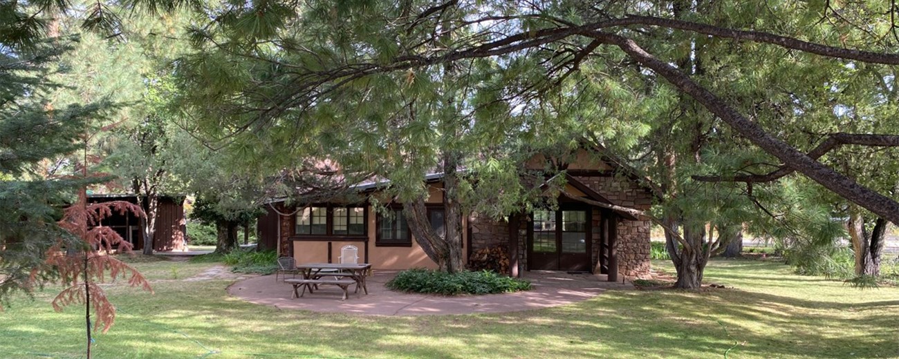 A one-story wood and stone house nestled among pine trees.