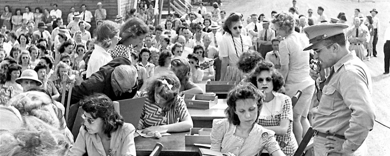 Oak Ridge workers sign up in 1944 Several men and women seated at outdoor desks with military personnel looking on.