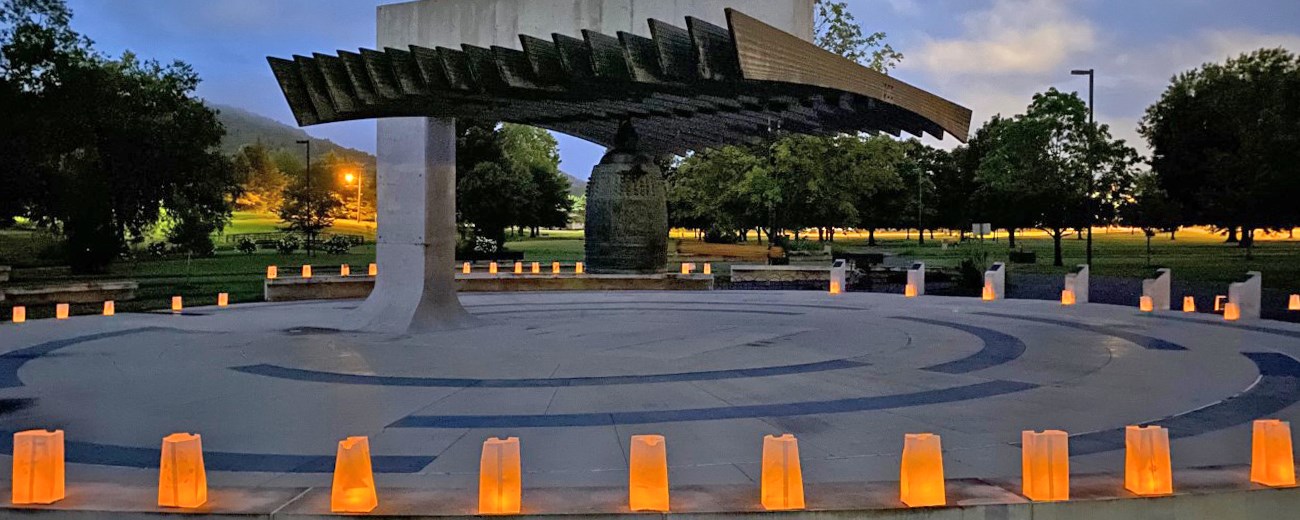 Luminarias surround a large bell suspended from a concrete structure.