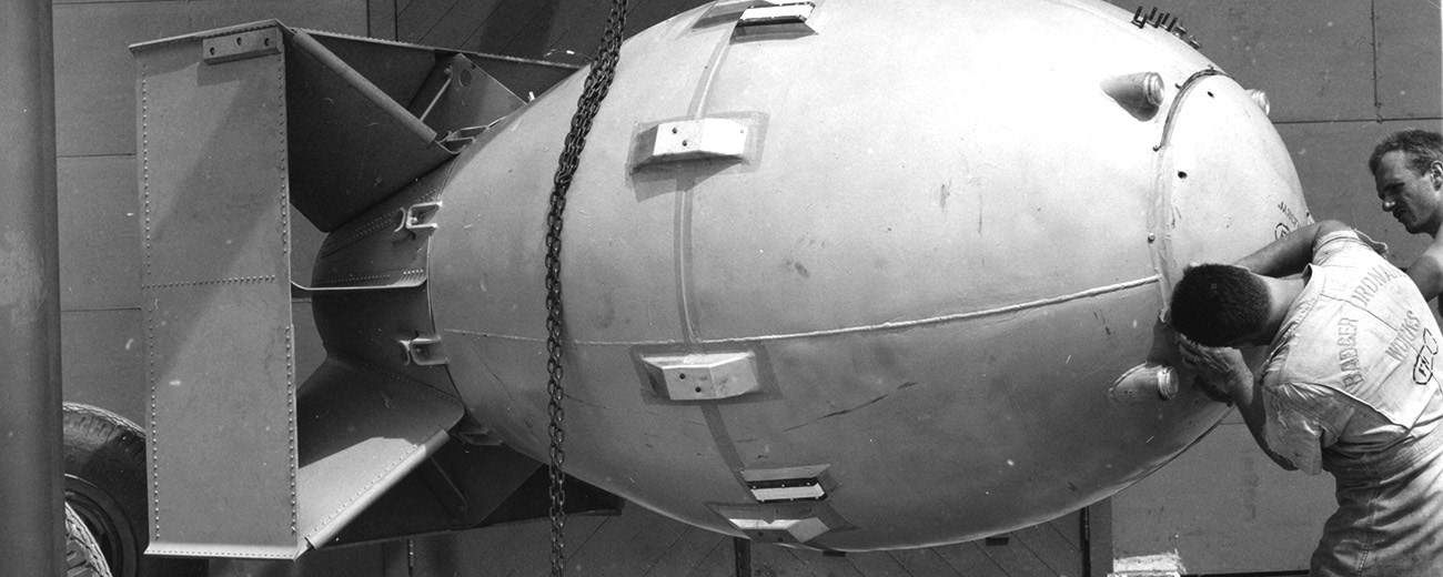 A black and white photo of a man working on a cylindrical object with a boxy tail.