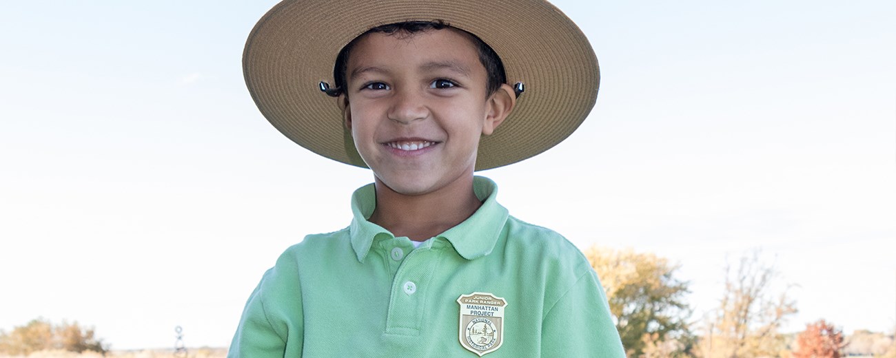 A young boy is wearing a ranger hat and a junior ranger badge on his shirt.