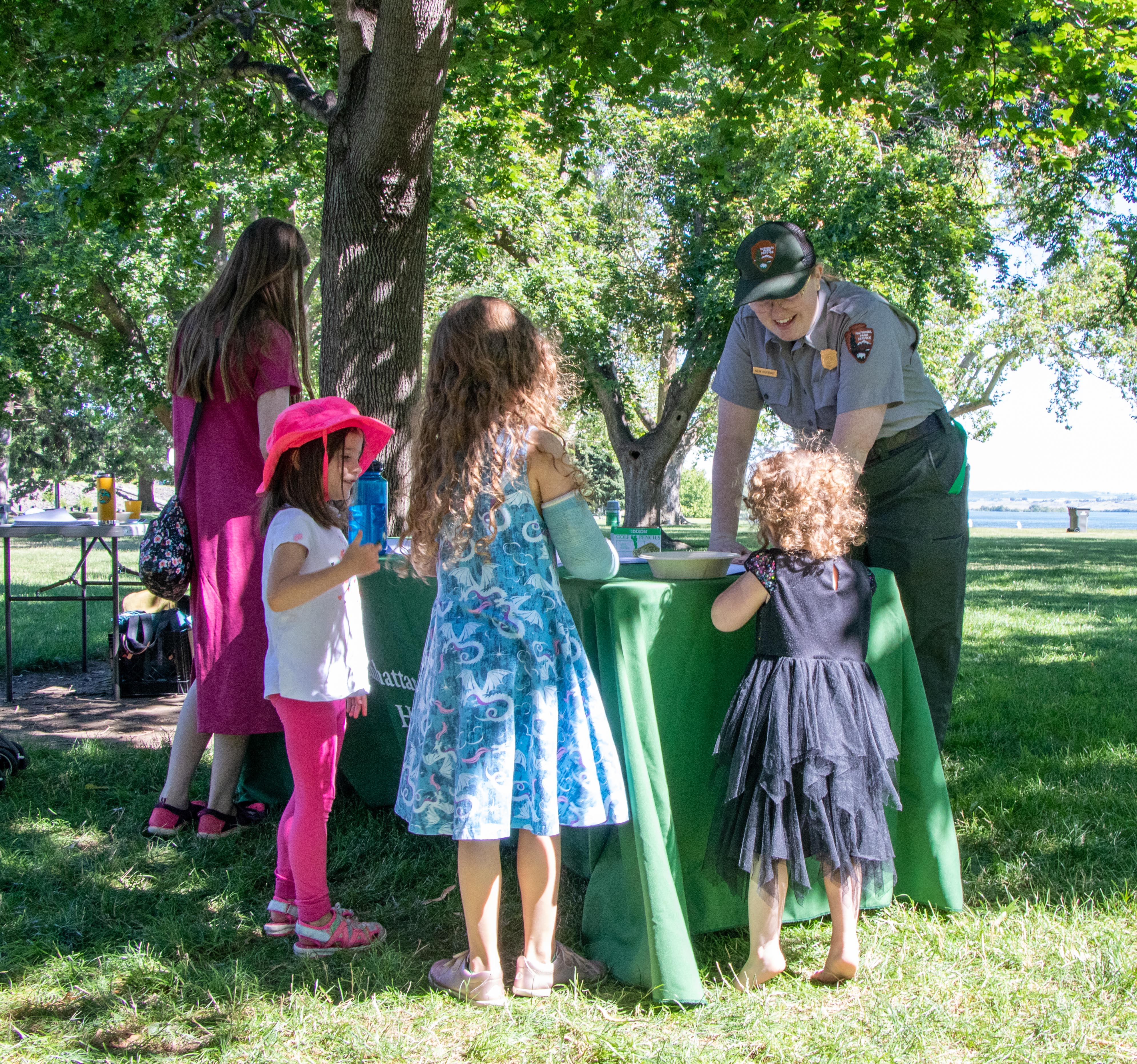 A woman in a ranger uniform talks with 4r children standing around a table outside.